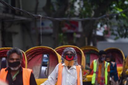 Conductores de bcictaxis, protegidos con mascarillas, esperan a clientes en Dhaka (Bangladés).