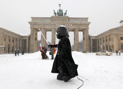 Un actor callejero, disfrazado del personaje de Darth Vader de <i>La Guerra de las Galaxias</i>, camina por la Puerta de Brandeburgo en medio de la nieve.