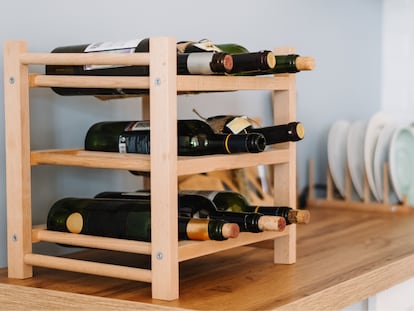 Conservar el vino en posición horizontal ayuda a mantener humedecido el corcho y prolonga su duración. En la foto, un estante de madera con varias botellas de vino.