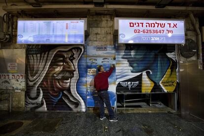 Un comerciante cierra las puertas de su establecimiento en el mercado Mahane Yehuda, decorado con un grafiti del artista callejero Solomon Souza, en Jerusalén. El grafitero de origen británico ha convertido el mercado principal del oeste de la ciudad en una galería de arte compuesta por un total de 150 grafitis creados en los últimos dos años dentro de su proyecto Shuk Gallery (galería del zoco).