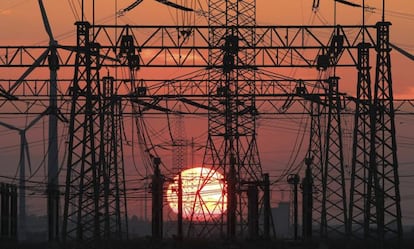 Torres de tendido eléctrico y molinos de viento durante un atardecer.