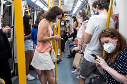 Un grupo de personas consulta sus teléfonos móviles en un vagón del metro de Madrid.