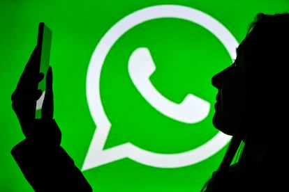 Una mujer sostiene un teléfono móvil ante un logo de WhatsApp, en enero de 2021, en Edmonton, Canadá.