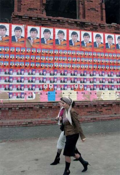 Dos mujeres caminan junto a un muro lleno de carteles electorales en Grozni.