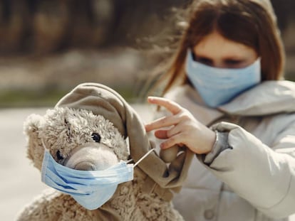 Una niña con mascarilla juega con su oso de peluche