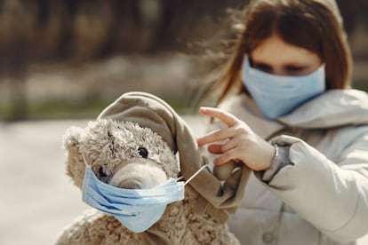 Una niña con mascarilla juega con su oso de peluche