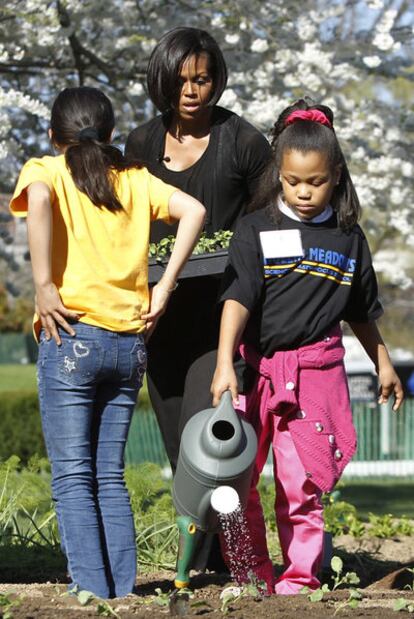 Michelle Obama y su hija Malia, con una regadera, junto a otra niña.