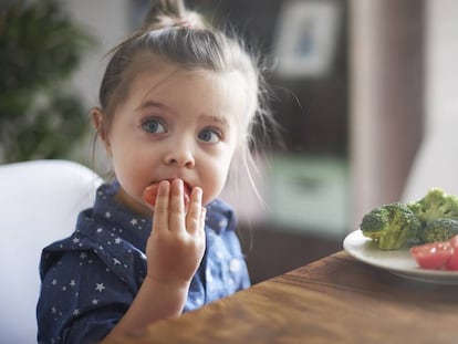 Una niña muerde un tomate.