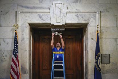 Joel Benowit, gerente de una sucursal de operaciones para instalaciones financieras de Estados Unidos, cuelga una placa con el nombre del gobernador demócrata de Kentucky, Andy Beshear, en su oficina en el edificio del Capitolio, poco después de su ceremonia de juramentación privada.