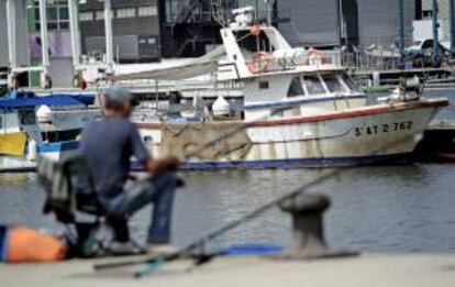 Un hombre pesca, este mediodía, en el puerto junto a los barcos de la Cofradía de Pescadores de Valencia.