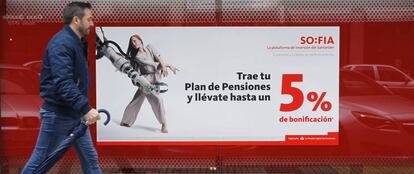 Una persona camina delante de una sucursal bancaria en la que se anuncian planes de pensiones.