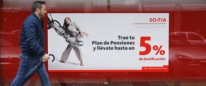 Una persona camina delante de una sucursal bancaria en la que se anuncian planes de pensiones. 