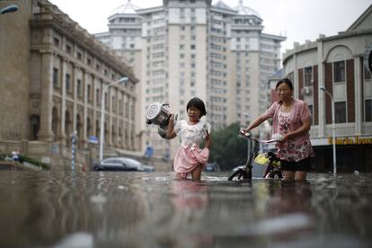 Una mujer y una niña cargan calderas a través de una calle inundada, en Tianjin, China, el martes 20 de julio. 