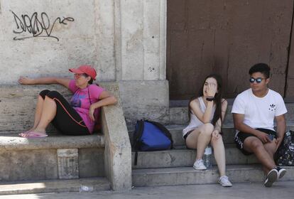 Tres personas a la sombra en la plaza de la Virgen de Valencia.