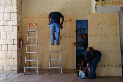 Trabajadores protegen con madera las ventanas de un comercio en Cancún. 
