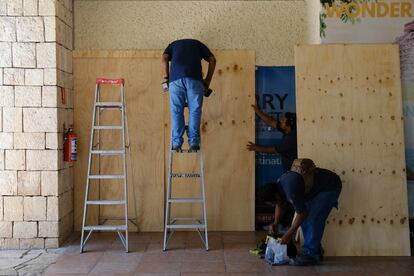 Trabajadores protegen con madera las ventanas de un comercio en Cancún. 