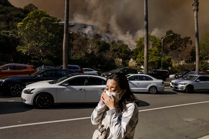 Una mujer habla por teléfono mientras evacúa un barrio amenazado por el incendio forestal de Palisades.