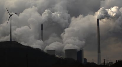 Chimeneas de una planta de carb&oacute;n alemana emiten humo junto a un molino de viento.