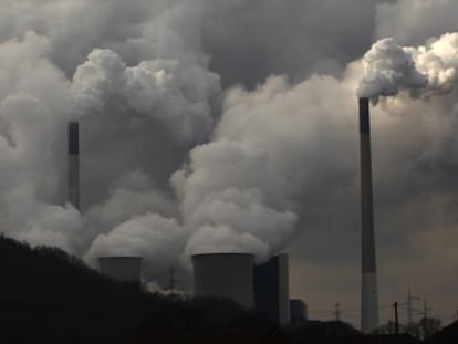 Chimeneas de una planta de carb&oacute;n alemana emiten humo junto a un molino de viento.