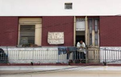 Una mujer permanece en el balcón de su vivienda junto a un cartel que anuncia su venta, en La Habana (Cuba). EFE/Archivo