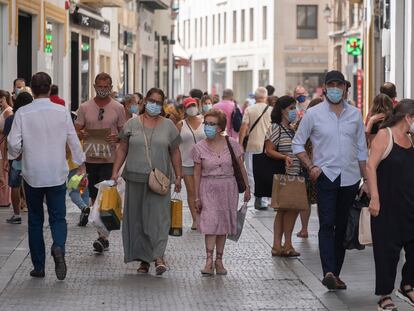 People wear face masks as they walk down the shopping strip in Seville.