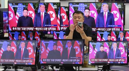 Un hombre atiende su teléfono móvil rodeado de pantallas que retransmiten la reunión entre Trump y Kim Jong-un, en Singapur.