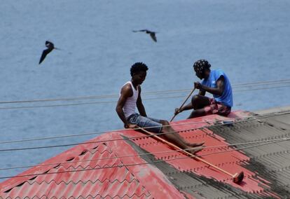 Dos hombres limpian las cenizas en el techo de una casa en Wallilabou, en el lado occidental de la isla caribeña de San Vicente, el lunes 12 de abril.