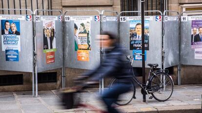 Una mujer pasea en bicicleta junto a varios carteles electorales en una calle de París, Francia, este lunes.