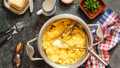 Una cazuela con puré de patatas, rodeada de un accesorio para triturar las patatas cocidas y algunos de los ingredientes más comunes, como leche y mantequilla.
