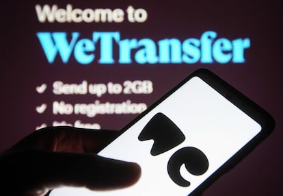 Un usuario maneja su teléfono frente a una pantalla con el servicio WeTransfer abierto.