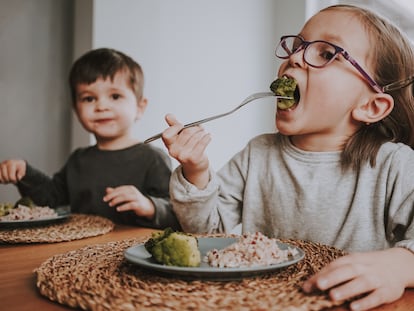 Siblings eat a healthy vegan lunch of broccoli and brown rice at home.