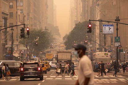 A man wears a mask as he crosses an intersection in a haze-filled sky of Manhattan, New York