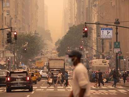 A man wears a mask as he crosses an intersection in a haze-filled sky of Manhattan, New York, on June 7, 2023.