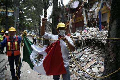 Dos rescatistas sostienen una bandera de M&eacute;xico junto a un edificio derrumbado.