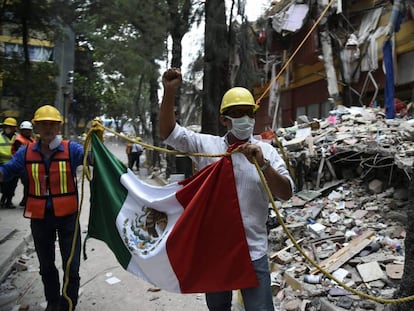 Dos rescatistas sostienen una bandera de México junto a un edificio derrumbado.