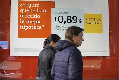 Dos personas pasan ante un cartel de promoción de una hipoteca, en Madrid.