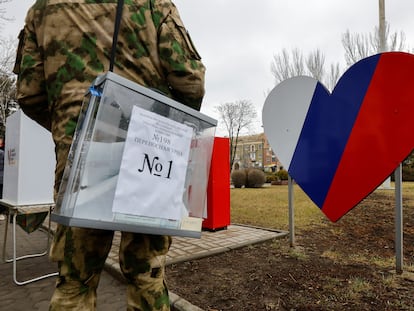 Un miembro en uniforme militar de la comisión electoral del territorio ocupado de Donetsk transporta una urna en un punto de voto situado en plena calle.