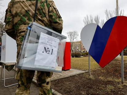 A military member of the electoral commission of occupied Donetsk carries a ballot box at a voting point located in the middle of the street.