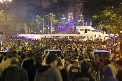 Miles de hinchas del Real Madrid rodean la fuente de Cibeles, vallada y protegida por la policía, con la Puerta de Alcalá al fondo.