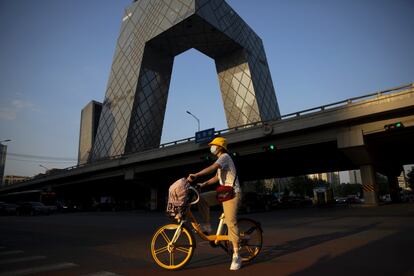 Una mujer cruza en bicicleta frente al edificio de la Televisión Central de China (CCTV), en Pekín. Las autoridades de la capital de China anunciaron el jueves que las mascarillas ya no serán obligatorias al aire libre.