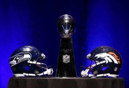 El trofeo Vince Lombardi (c) flanqueado por el casco de los Seattle Seahawks (izq) y el de los Denver Broncos (dcha) antes del inicio de la rueda de prensa de los entrenadores de la Super Bowl XLVIII en Nueva York (Estados Unidos) este viernes 31 de enero de 2014.