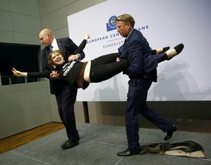 Dos agents de seguretat s'emporten per força la dona que ha saltat sobre la taula on estava Mario Draghi i la cap de premsa. Ella sortia fent el gest de victòria amb la mà.