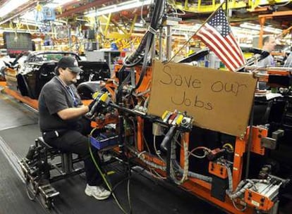 Un empleado de General Motors ensambla partes de un Corvette ante un cartel en el que pide que se salven los puestos de trabajo.
