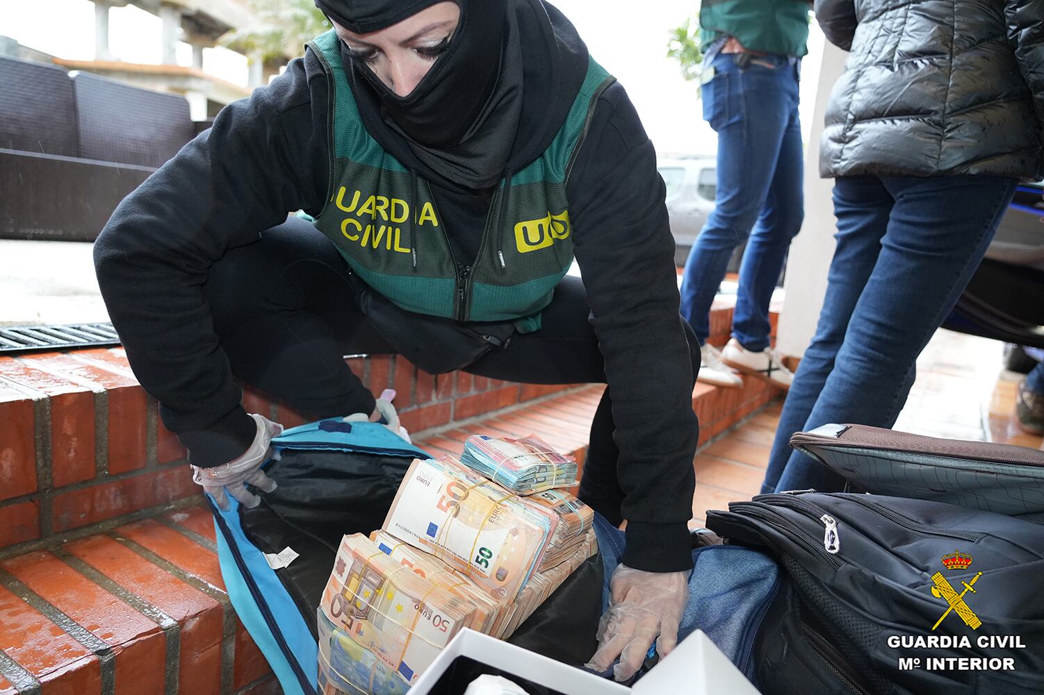 Una agente de la UCO inspecciona una mochila repleta de fajos de billetes intervenida durante la Operación Halia.