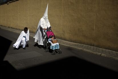 Un penitente de la hermandad de La Paz acompañado por dos niños se dirige a una procesión el Domingo de Ramos en Sevilla.