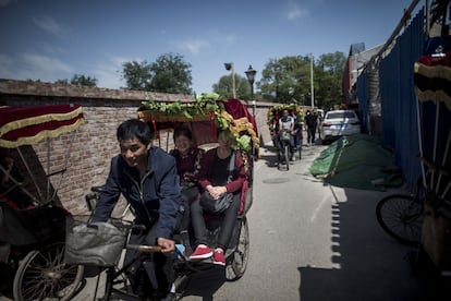 Dos clientes viajan en bicitaxi por Pekín.