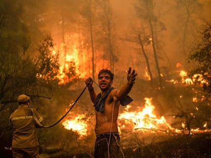 Un residente de la localidad de Pefki, en la isla de Eubea, hace un gesto mientras sostiene una manguera de agua vacía durante un intento de extinguir los incendios forestales que golpean a Grecia desde hace días.