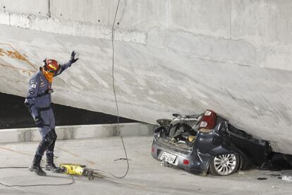 Un trabajador de los servicios de emergencia se acerca al coche aplastado bajo el viaducto.