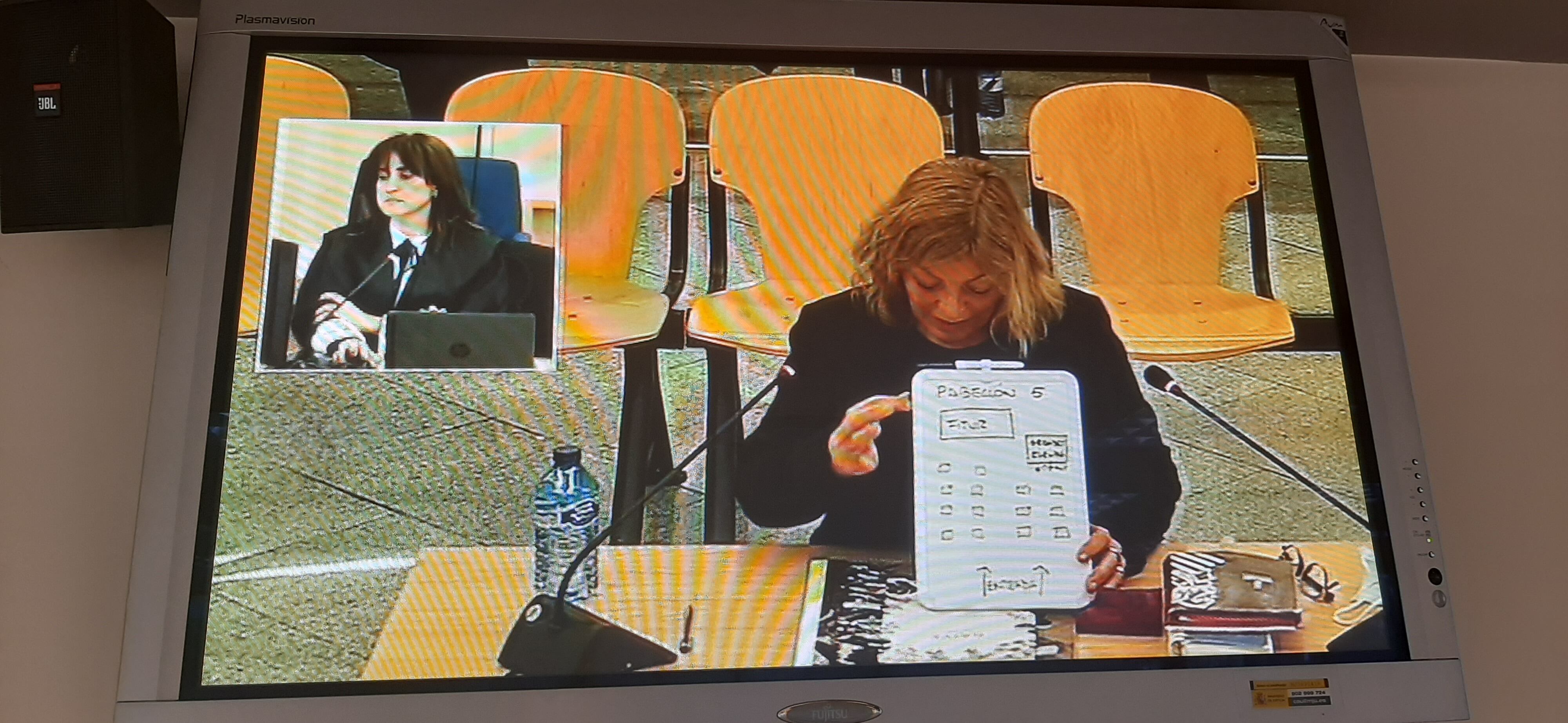 La acusada Salvadora Ibars, durante su declaración este miércoles en el juicio, con una pizarra sobre los puestos de Fitur, en uno de los monitores de la Audiencia Nacional.