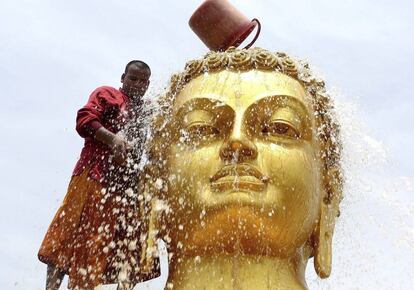 Un monje budista limpia una estatua de Buda.